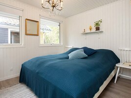 A bedroom with a bed, a chandelier, a window, a mirror, and a shelf with a plant.