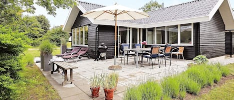 A modern house with a covered patio, outdoor seating, and a barbecue area.