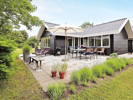 Een modern huis met een overdekte patio, zitplaatsen buiten en een barbecueplek.