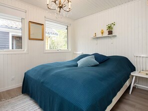 A bedroom with a bed, a chandelier, a window, and a shelf with a plant.