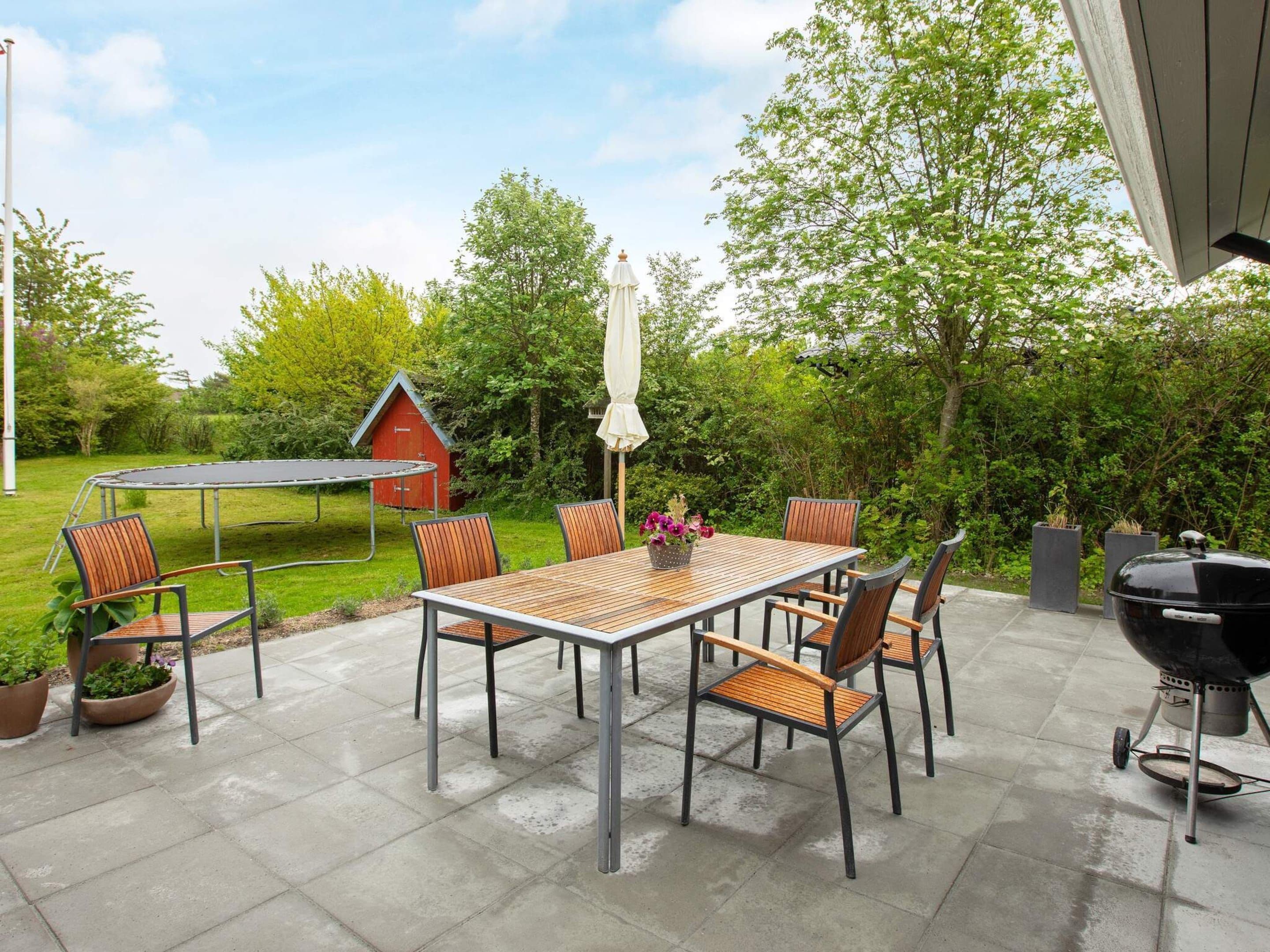 An outdoor patio with a table and chairs, a barbecue grill, and a trampoline.
