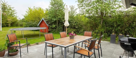 An outdoor patio with a table and chairs, a barbecue grill, and a trampoline.