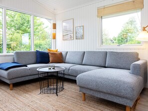 A modern living room with a grey sectional sofa, a round coffee table, and a large window offering a view of greenery.