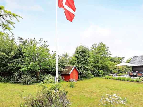 A red building with a white fence, surrounded by greenery and a flagpole with a flag.