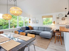 A modern living room with a grey sectional sofa, a dining table with placemats, and a kitchen area with a wooden countertop and stools.