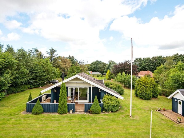 A single-story house with a sloped roof, a covered patio with outdoor furniture, and a flagpole in the yard.