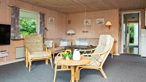 A cozy room with wooden walls, a sofa, two chairs, a small table with a vase of flowers, a lamp, and a TV. - 6 Person Holiday Home in Oksbol-by Traum (Oksbol)