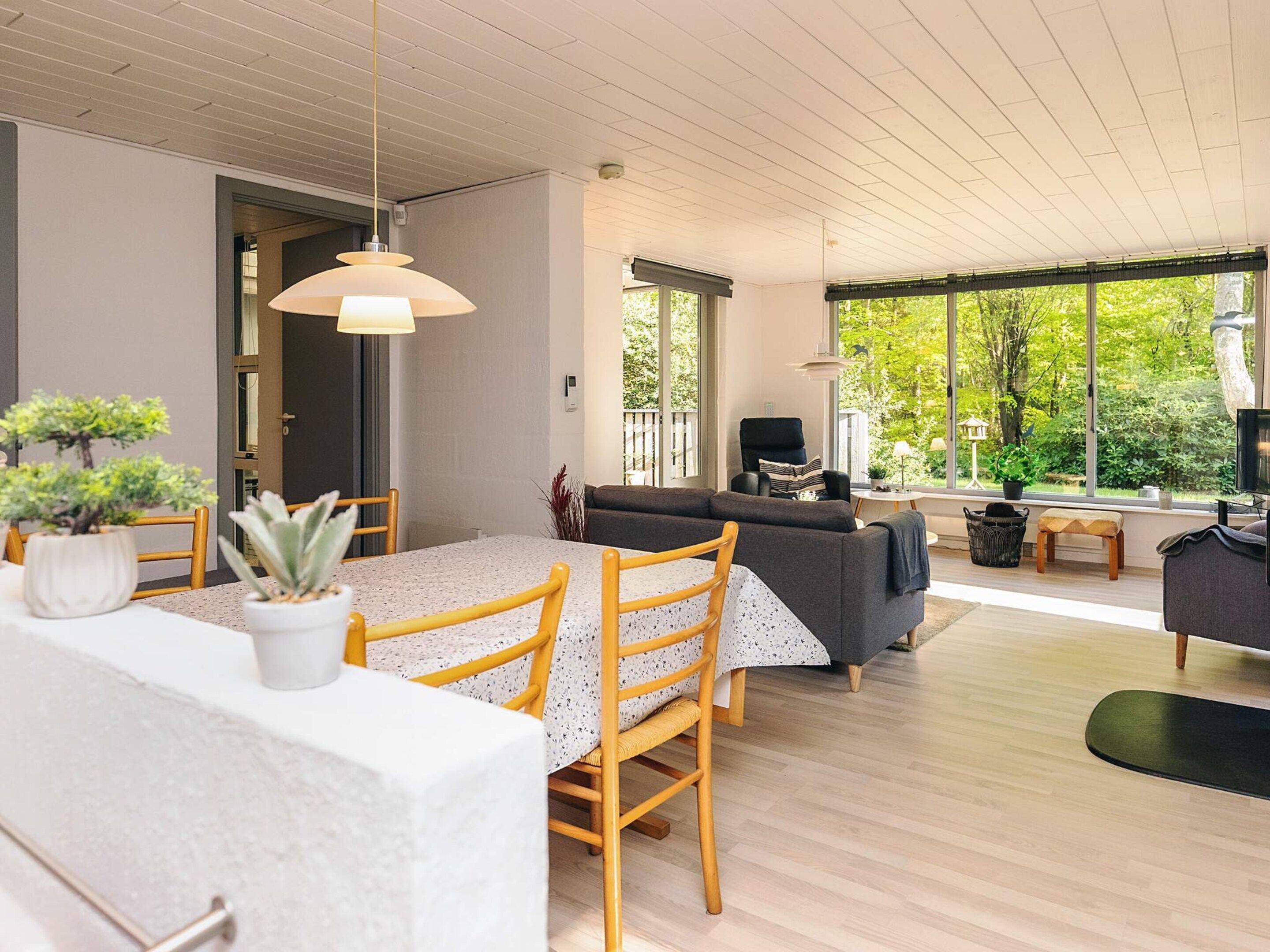 Un espacio moderno con comedor, sofá y ventanas amplias que ofrecen vistas al verdor.