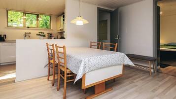 Una cocina moderna con comedor, sillas de madera, una mesa con mantel blanco y una lámpara colgante.
