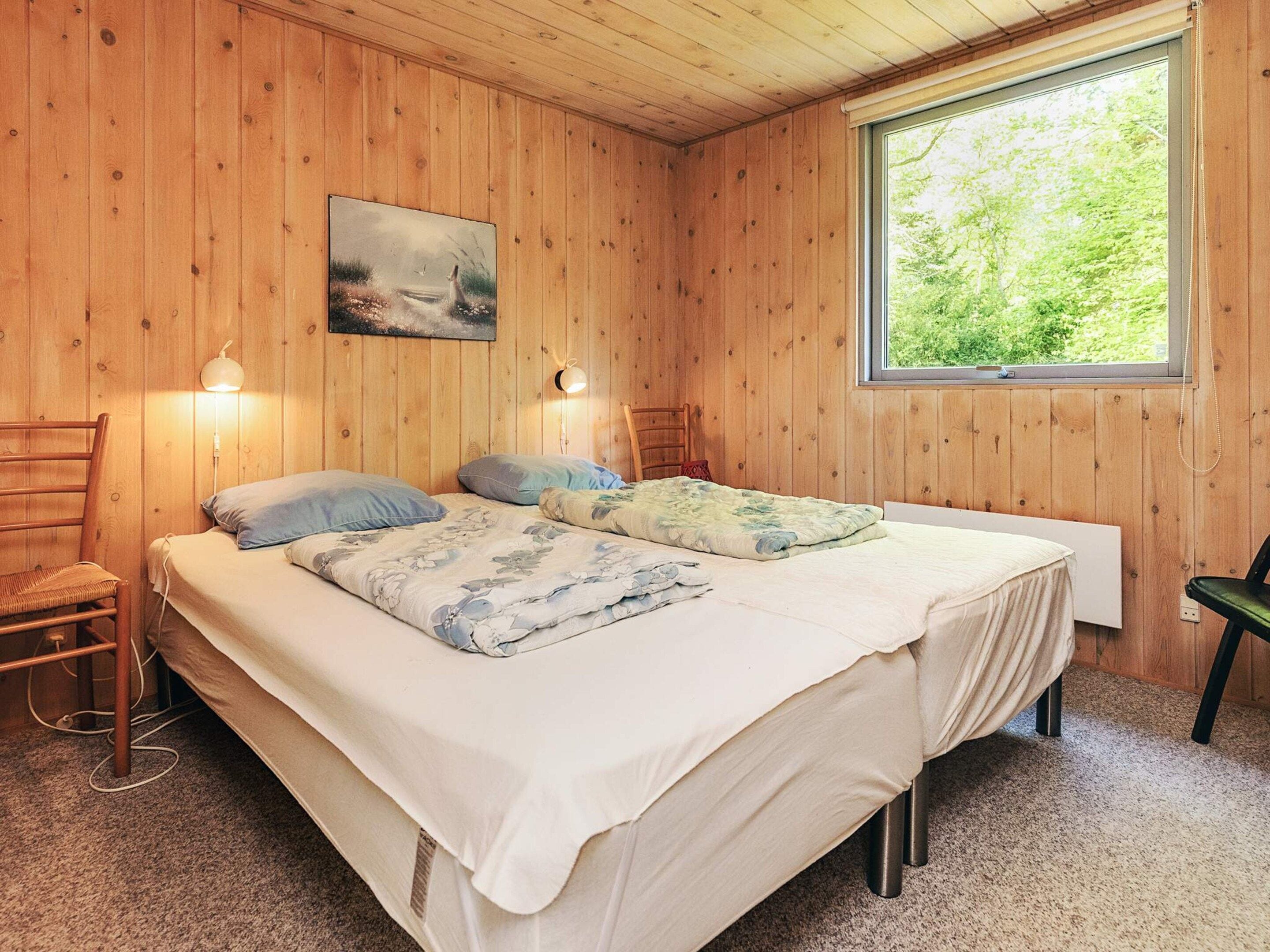 Una habitación con paneles de madera, una cama, dos lámparas de pared, un ventanal y un cuadro en la pared.