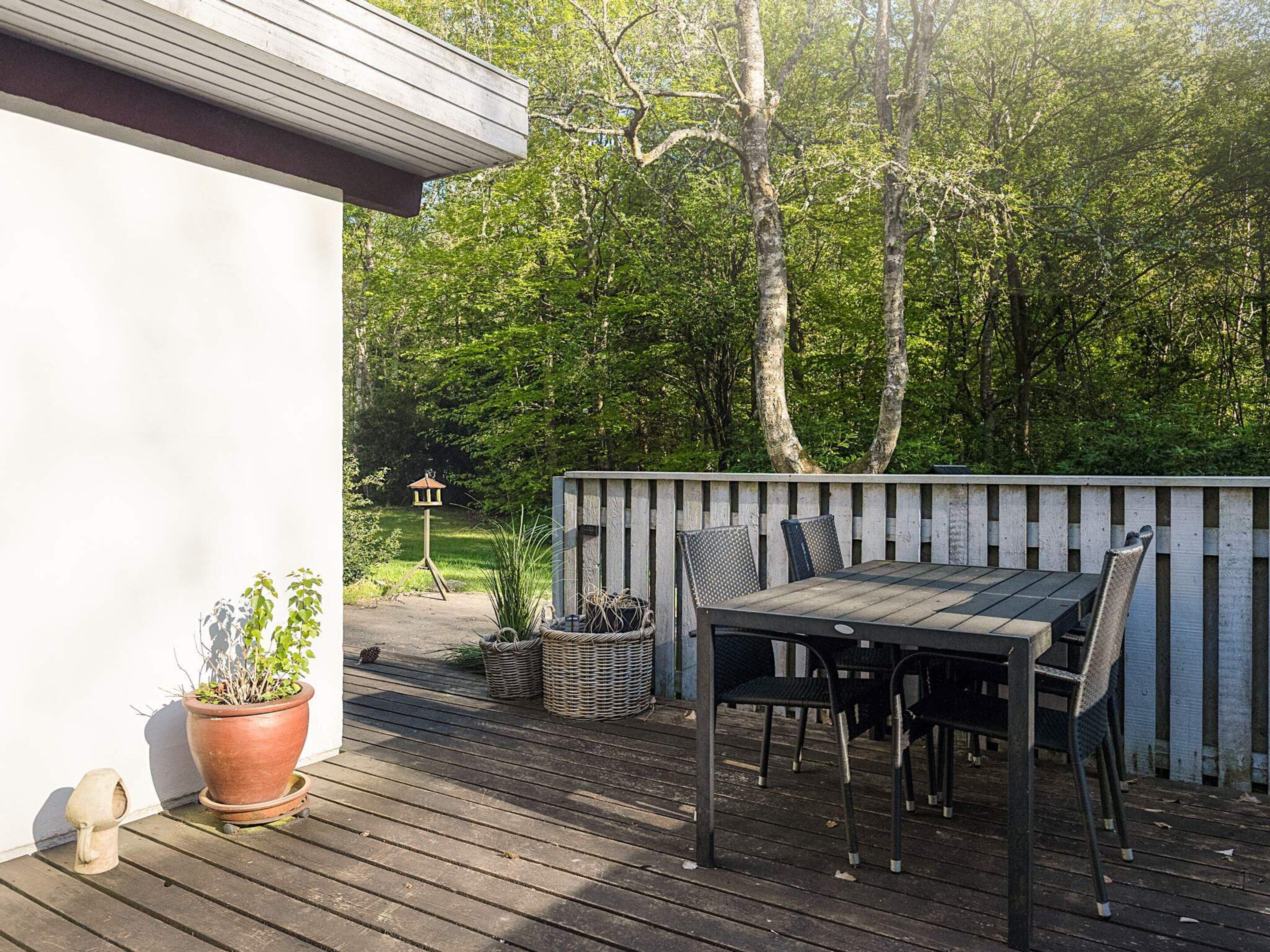 An outdoor deck with a wooden table and chairs, surrounded by a white fence and trees.