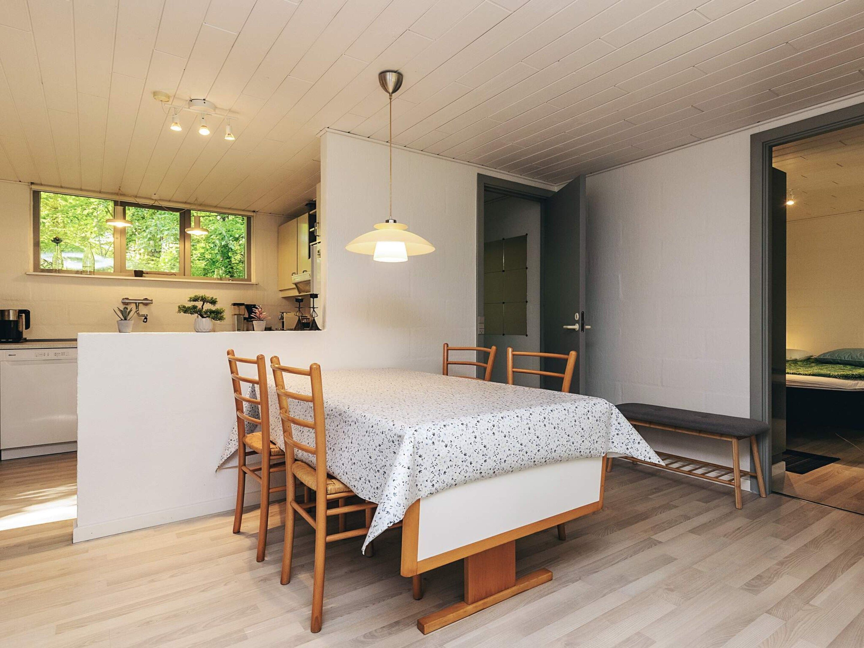 A modern kitchen with wooden cabinets, a dining table with chairs, and a pendant light.
