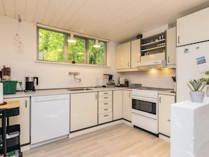A modern kitchen with white cabinets, a dishwasher, a stove, and a sink. There is a window providing natural light and a view of greenery outside.