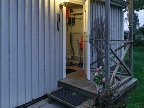 Ett trähus med en metalldörr, ett trappsteg som leder upp till ingången och en trädgårdsdel med en krukväxt.