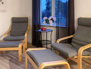 A room with two armchairs, a small table with two red candles, and a window with pink flowers.