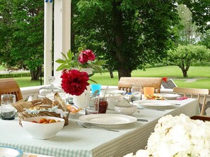 An outdoor dining table set with plates, glasses, and a vase of flowers.