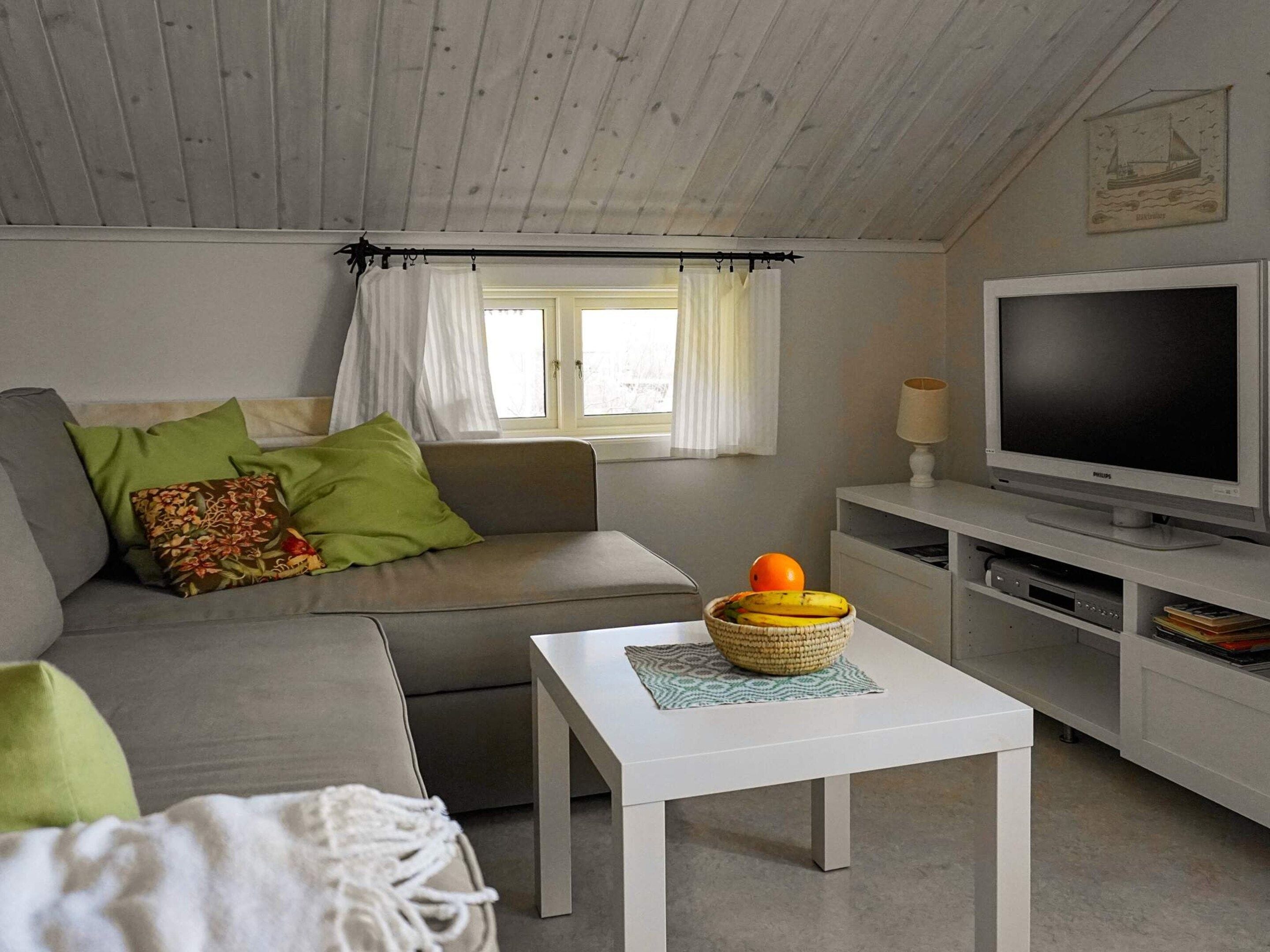 A modern living room with a grey sofa, a white coffee table, a television, and a window with curtains.