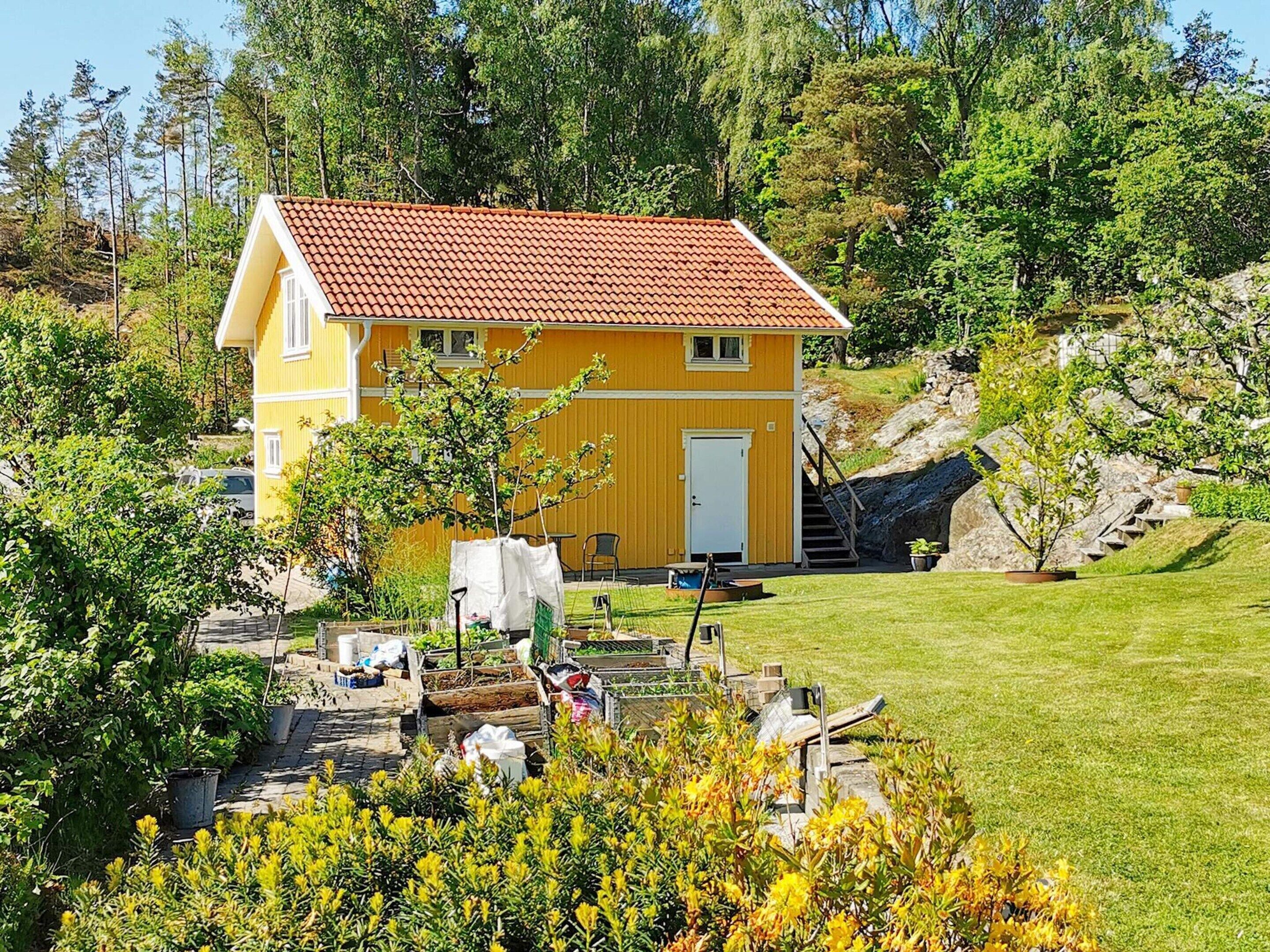 A yellow house with a red roof, surrounded by greenery and a small garden.