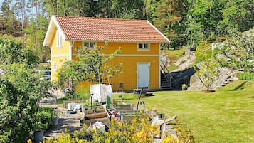 A yellow house with a red roof, surrounded by greenery and a small garden.