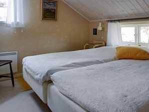 Een kamer met twee bedden, een stoel, een radiator, een raam met gordijnen en een schilderij aan de muur.