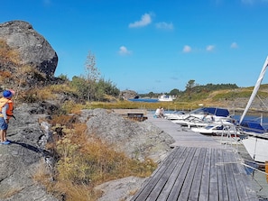 Een rotsachtige kustlijn met een houten steiger die uitkomt op een jachthaven met verschillende zeilboten.