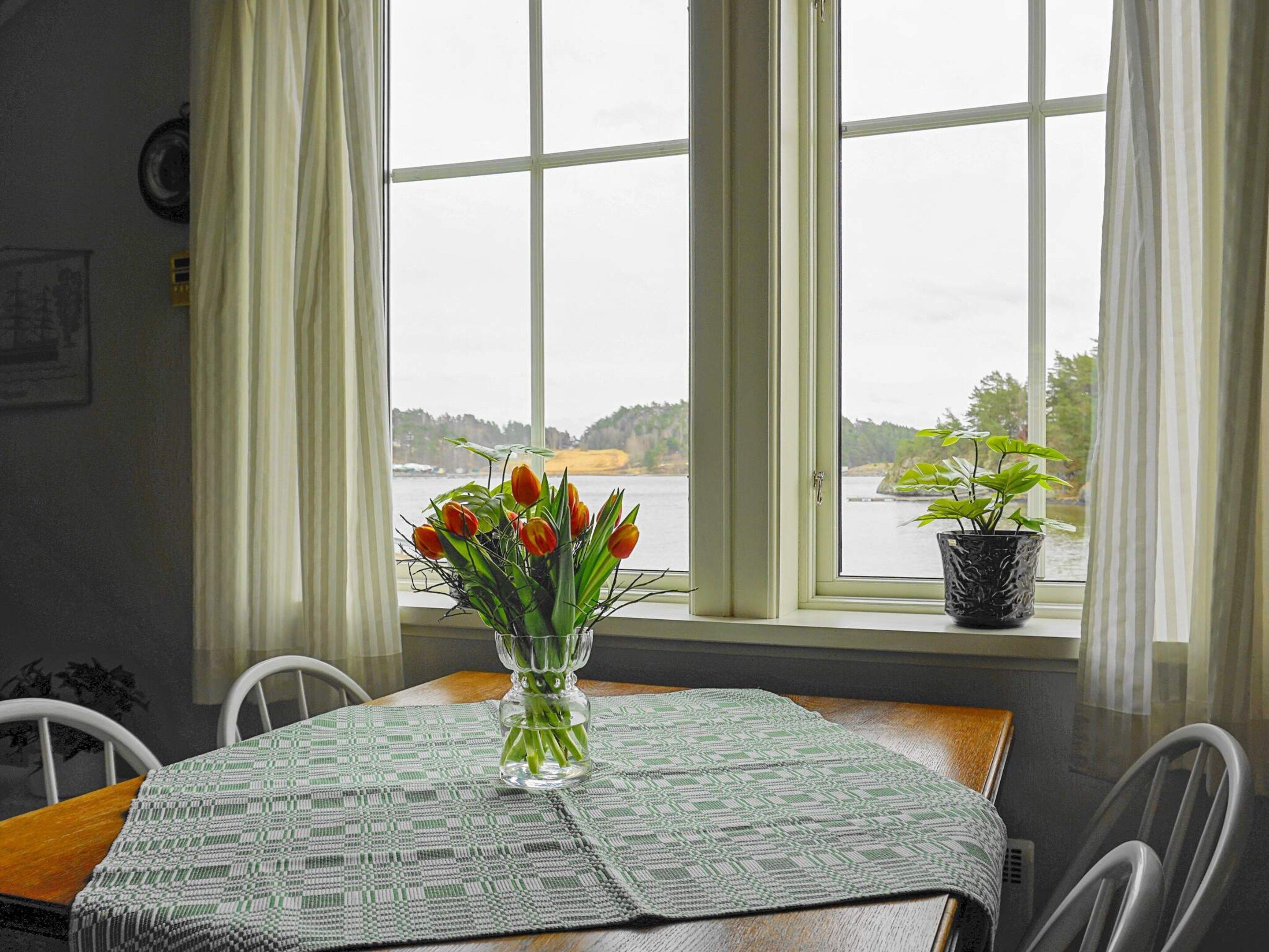 A dining table with a patterned tablecloth, a vase with tulips, and a potted plant on a windowsill.