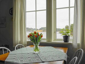 A dining table with a patterned tablecloth, a vase with tulips, and a potted plant on a windowsill. - 4 Star Holiday Home in Ellos (Ellos)