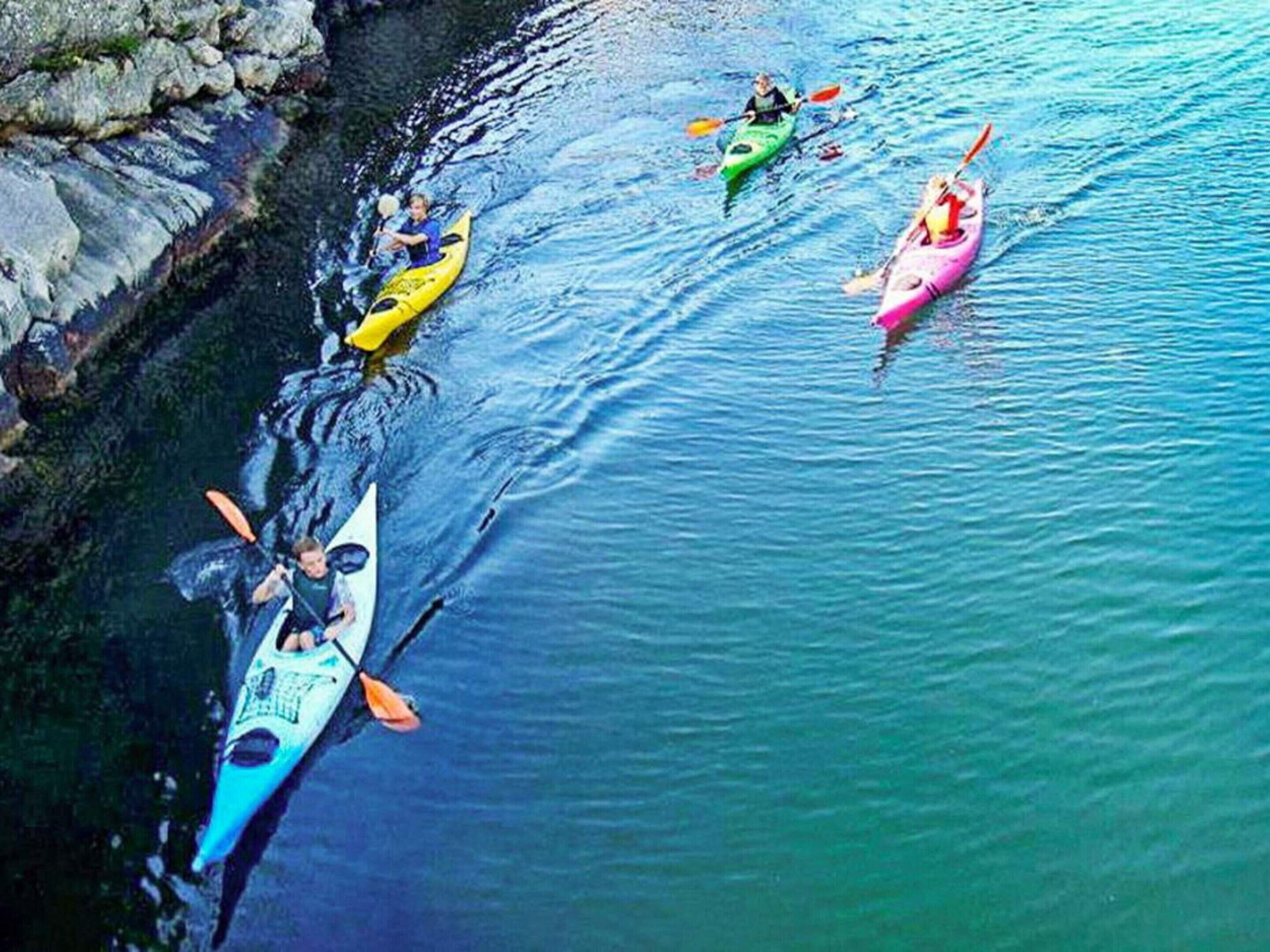 A group of kayaks on calm water near a rocky shoreline.