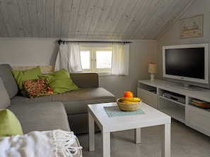 Een moderne woonkamer met een grijze bank, een witte salontafel, een televisie en een raam met gordijnen.