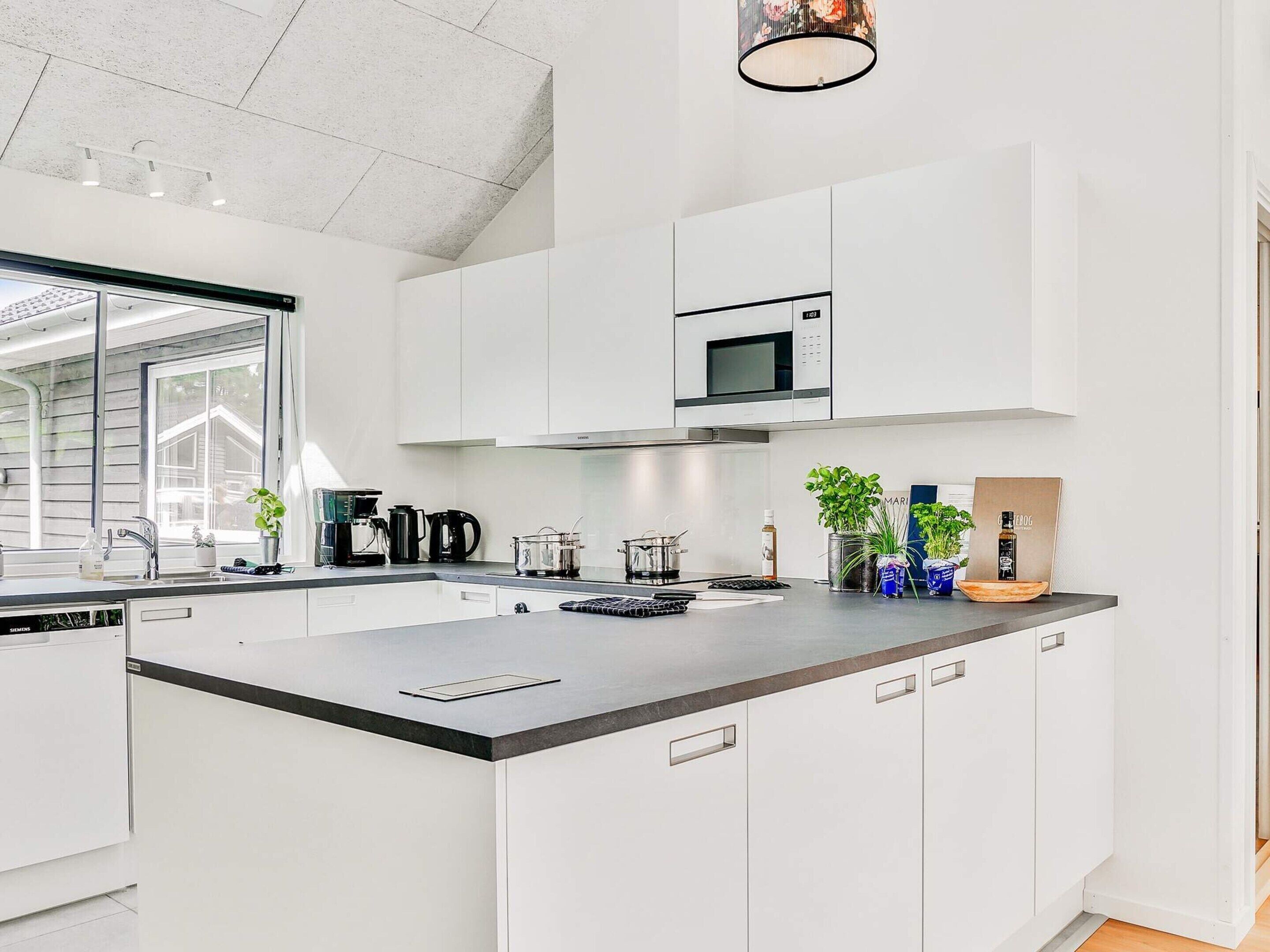 A modern kitchen with white cabinetry, a black countertop, and a built-in microwave.