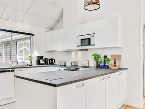 A modern kitchen with white cabinetry, a black countertop, and a built-in microwave. - 5 Star Holiday Home in Vaeggerlose (Vaeggerlose)