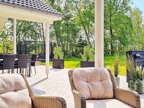 An outdoor patio with wicker furniture, a covered seating area, and a view of a green landscape. - 5 Star Holiday Home in Vaeggerlose (Vaeggerlose)