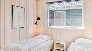 A room with two beds, a framed picture, a wall-mounted lamp, and a window with a view.
