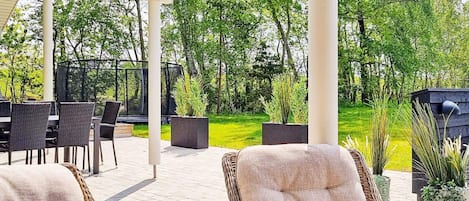 An outdoor patio with wicker furniture, a covered seating area, and a view of a lush garden.