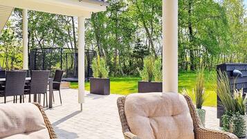 An outdoor patio with wicker furniture, a covered seating area, and a view of a green landscape.