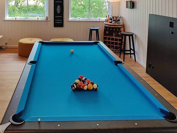 A pool table with balls, a bar area, and a window with a view of greenery.