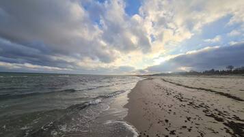 A beach with waves, a sandy shore, and a partly cloudy sky.