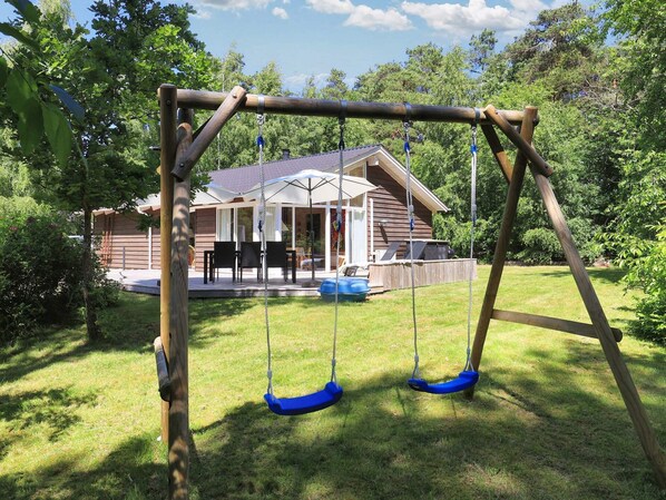 Un portique en bois installé dans un jardin, avec une maison en arrière-plan.
