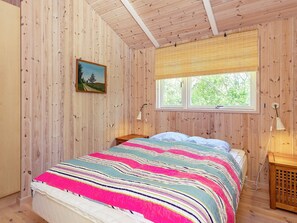 Une chambre avec des murs en bois, un lit recouvert d’une couverture à rayures colorées, une fenêtre avec des stores et un tableau accroché au mur.