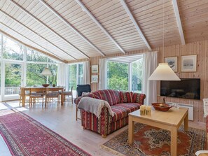Un salon chaleureux avec un plafond en bois, un canapé, un téléviseur et un coin repas comprenant une table et des chaises.