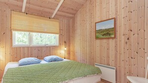 A wooden-paneled room with a bed, a window, a wall-mounted picture, and a white chair.