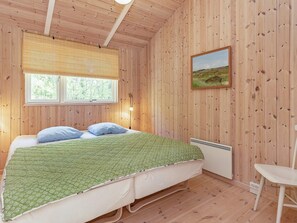 Une pièce aux murs lambrés, comprenant un lit, une fenêtre, un tableau accroché au mur et une chaise blanche.