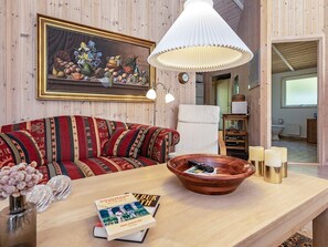 Une pièce chaleureuse avec un mur en bois, un canapé à motifs, une table en bois sur laquelle se trouve un bol, une lampe et un tableau encadré.