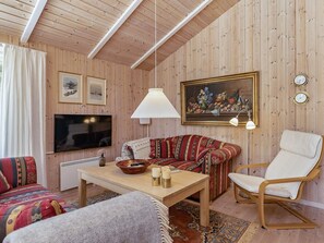 Un salon confortable avec un canapé, un fauteuil, une table, un téléviseur et un tableau.