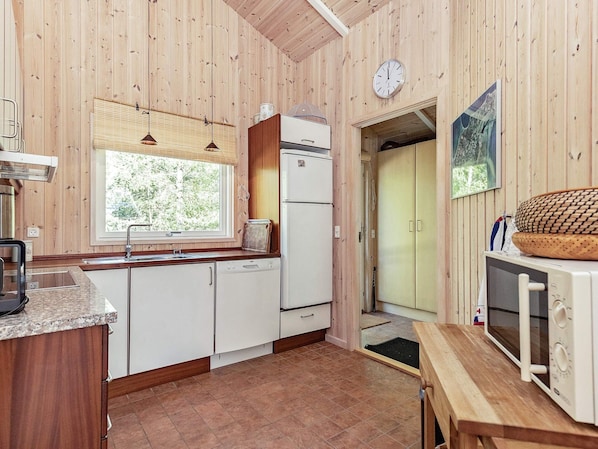 A kitchen with wooden walls, a window, a refrigerator, a sink, and a microwave.