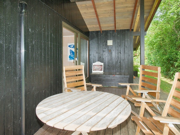 A wooden deck with a round table and four chairs, a black wall with a poster, and a wooden ceiling.