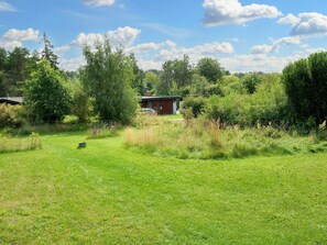 A grassy field with a red building, surrounded by trees and vegetation.