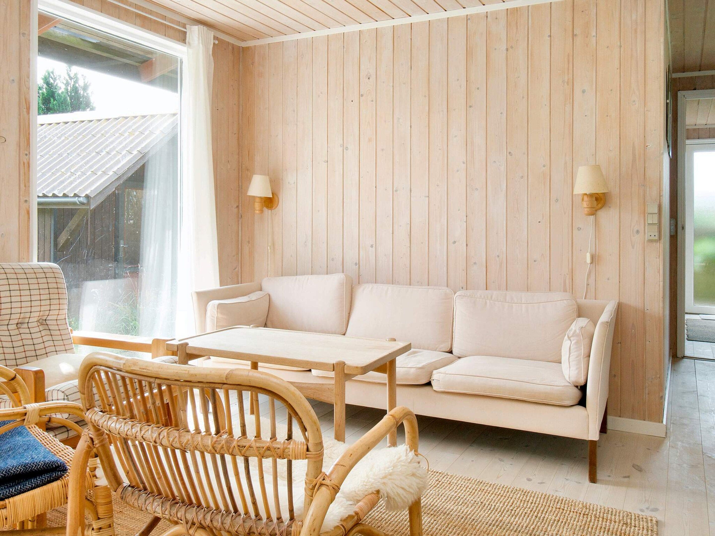 A room with a wooden paneled wall, a white sofa, a wooden table, and wicker furniture.