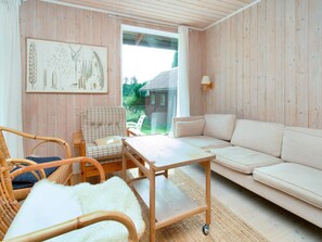 A cozy room with a wooden wall, a white sofa, a wicker chair, a small table, and a framed botanical illustration. - 6 Person Holiday Home in Farevejle (Faarevejle)