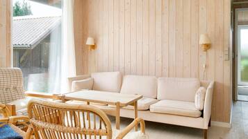 Una habitación con pared de madera, un sofá blanco, una mesa de madera y sillas de mimbre.